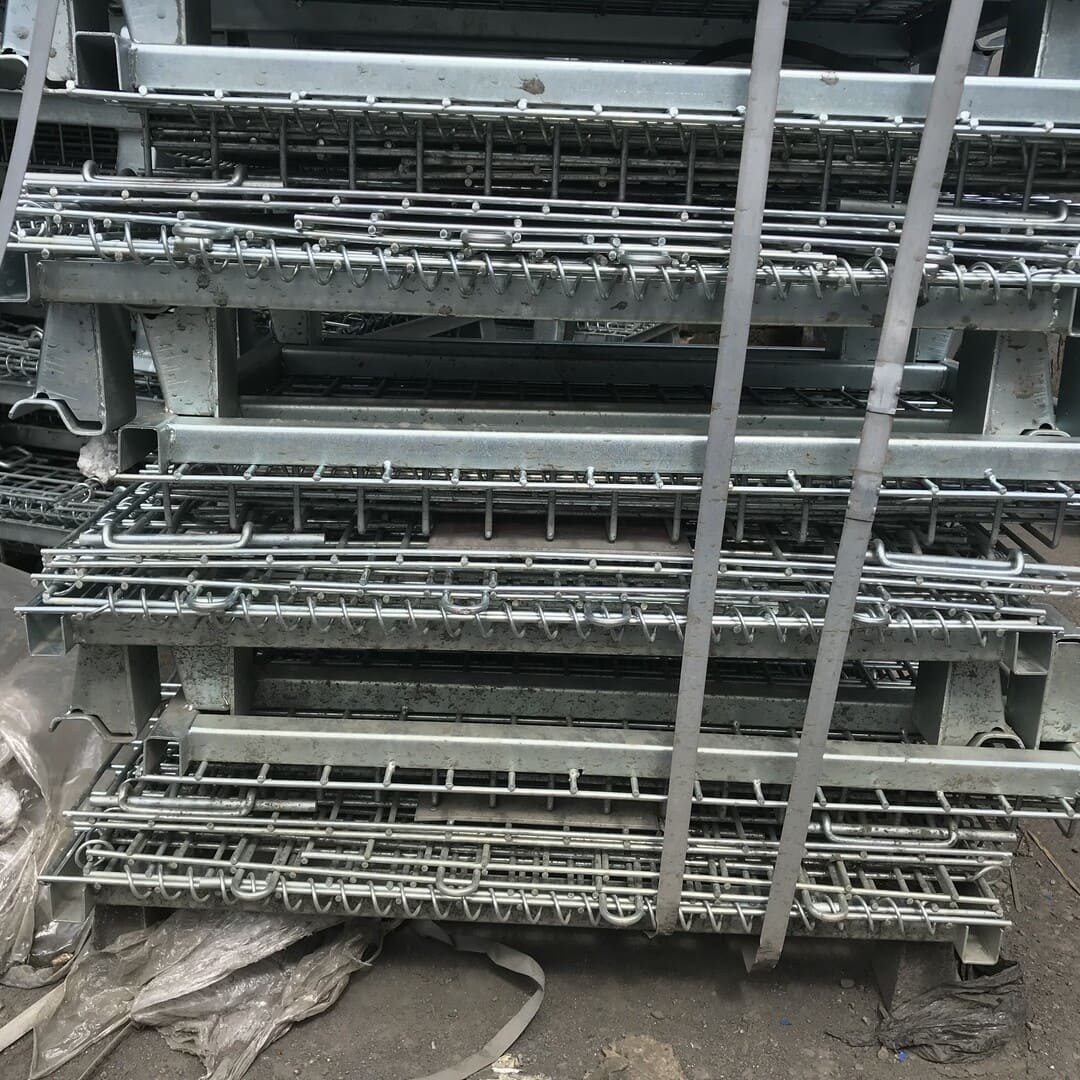 Unpainted used galvanised collapsible metal pallet cages stacked in a warehouse.