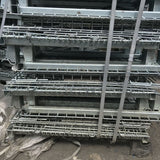 Unpainted used galvanised collapsible metal pallet cages stacked in a warehouse.