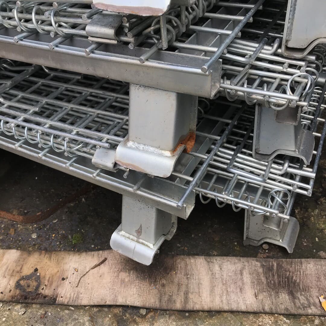 Used unpainted collapsible mesh pallet cages stacked inside warehouse.